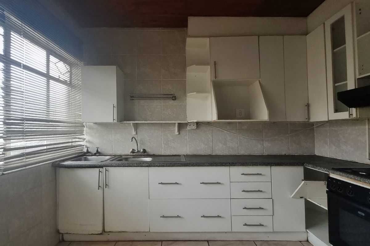 A dated kitchen featuring white cabinetry, laminate countertops, a built-in oven and hob, and tiled finishes, offering potential for a modern renovation.