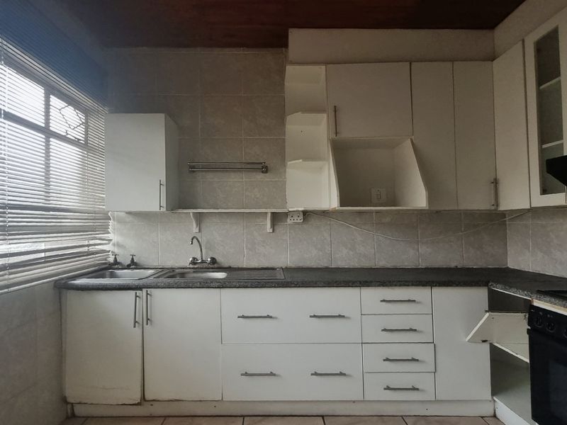A dated kitchen featuring white cabinetry, laminate countertops, a built-in oven and hob, and tiled finishes, offering potential for a modern renovation.