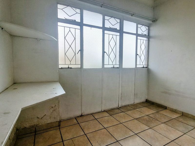A vacant utility space featuring tiled flooring, built-in shelving, and large metal-framed windows, offering a functional area for laundry or storage needs.