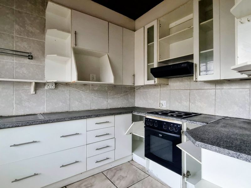 A functional kitchen featuring built-in cabinetry, a hob, oven, and extractor fan, requiring some maintenance and repairs to the cabinetry and finishes.