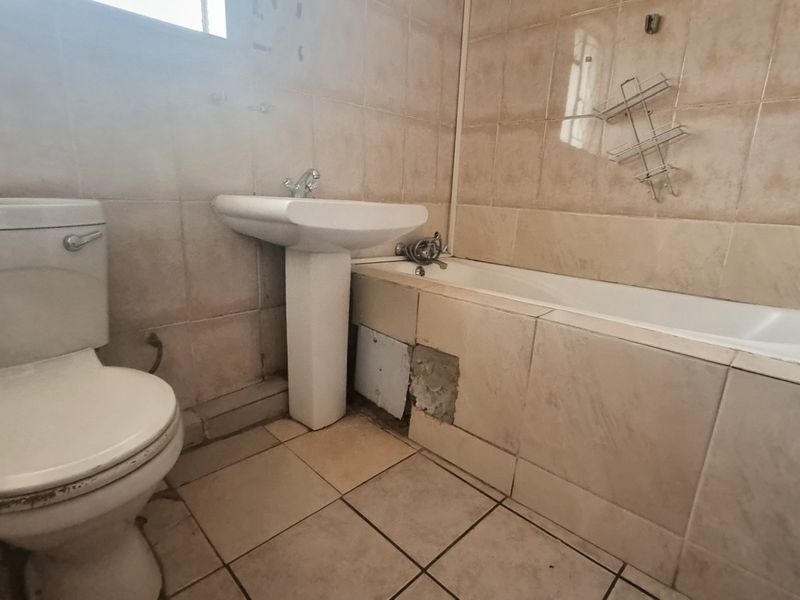 A dated bathroom featuring a pedestal basin, toilet, and bathtub with tiled finishes, currently requiring maintenance and cosmetic updates to the bathtub panel.