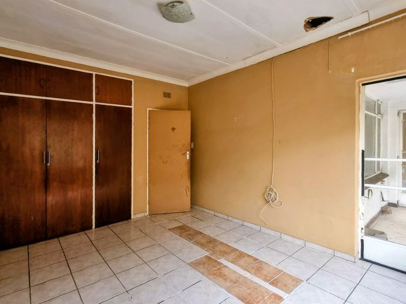 An empty bedroom featuring built-in wooden cupboards, tiled flooring, and a ceiling light fixture, requiring cosmetic updates and repairs to the ceiling and walls.
