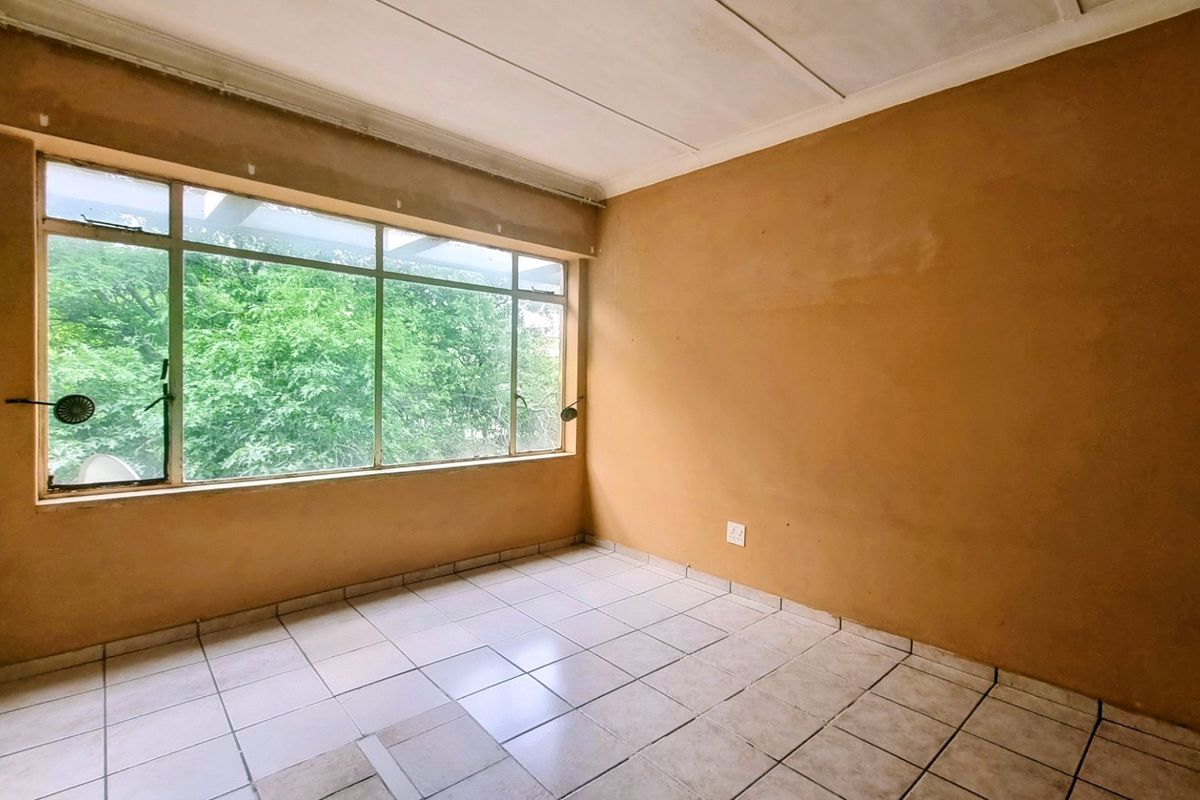 An empty bedroom featuring tiled flooring and a large window, offering a blank canvas for renovation and interior design updates.