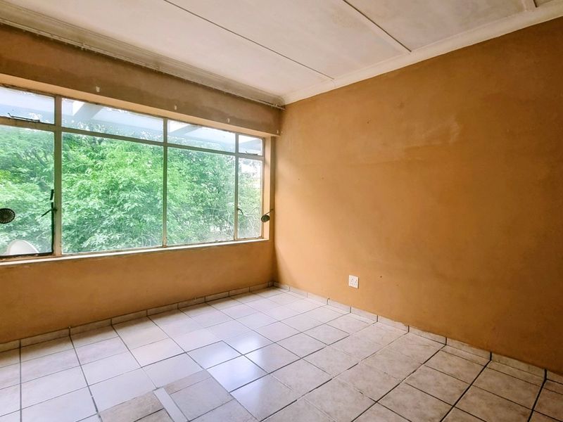 An empty bedroom featuring tiled flooring and a large window, offering a blank canvas for renovation and interior design updates.