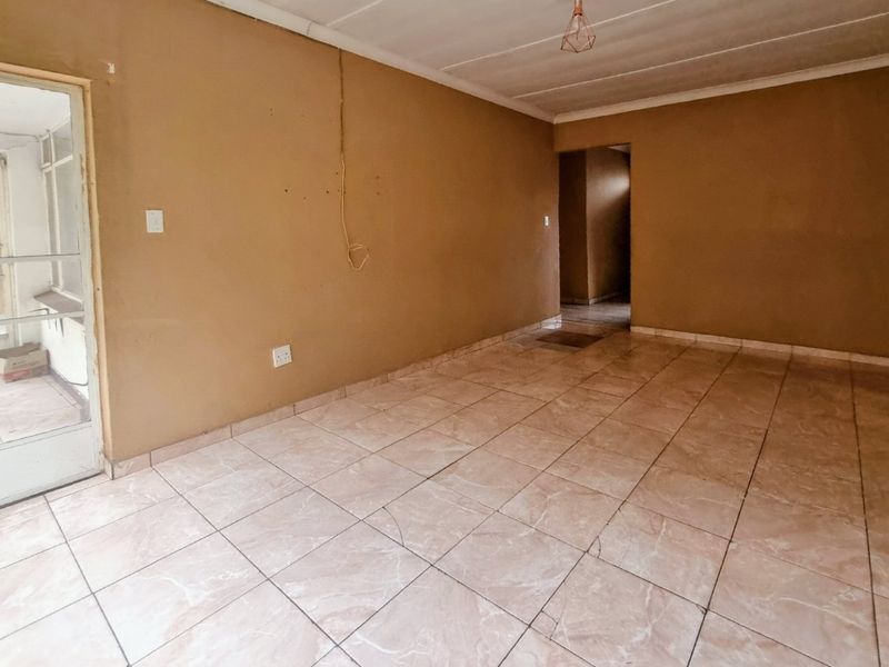 An empty living room featuring tiled flooring and a glass panel door leading to an adjacent space, requiring cosmetic updates to improve its appeal.
