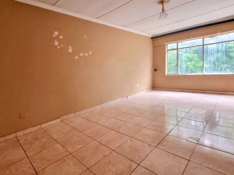 An empty living room featuring tiled flooring, a large window, and a ceiling light fixture, requiring cosmetic updates to the walls and flooring.