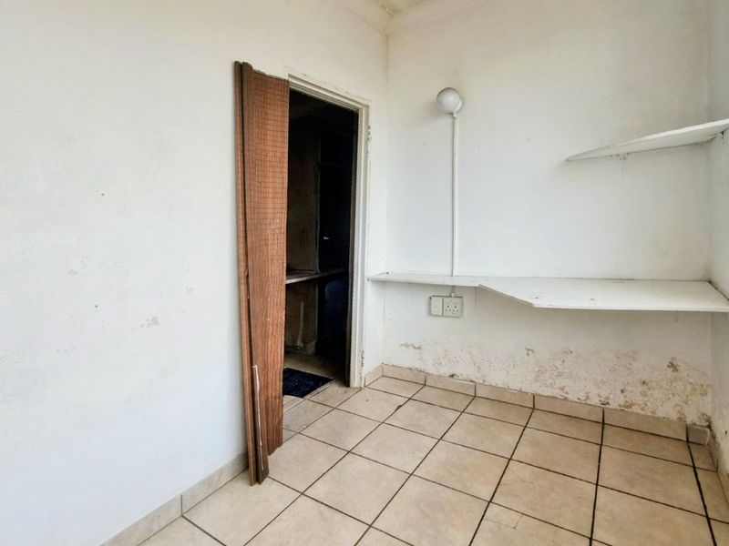 A small utility or storage area featuring tiled flooring, built-in shelving, and electrical points, currently requiring maintenance and cosmetic updates.