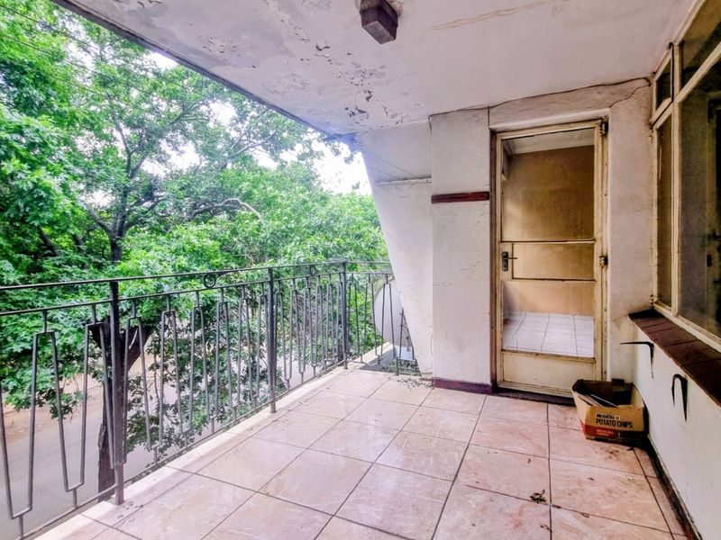 A covered balcony featuring tiled flooring and a wrought iron railing, offering an outdoor space in need of cosmetic refurbishment.