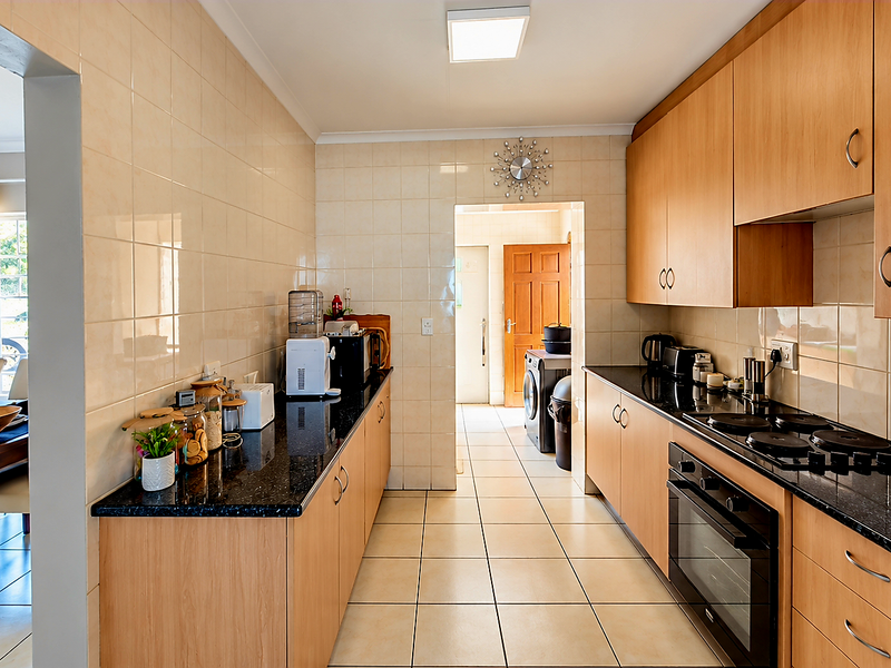 A functional kitchen featuring light wood cabinetry, dark granite countertops, integrated electric hob and oven, and neutral tiled splashbacks and flooring.
