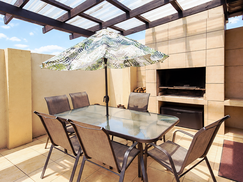 Covered outdoor patio featuring a built-in braai, tiled flooring, and a timber pergola, providing an ideal space for alfresco dining and entertaining.