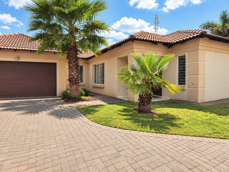 Front elevation of a townhouse featuring a paved driveway, roller garage door, and well-maintained exterior facade with landscaped garden.