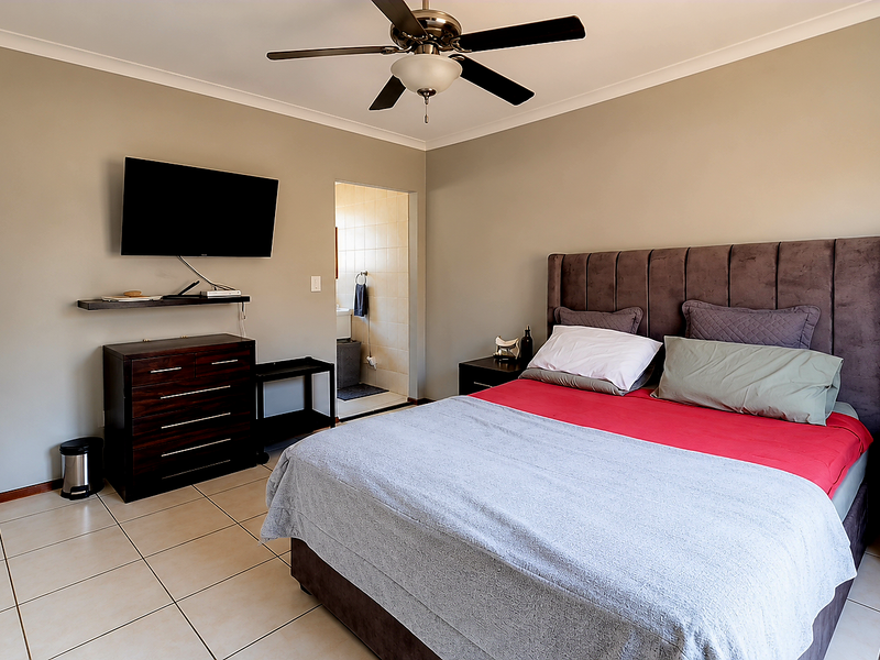 A well-maintained bedroom featuring tiled flooring, a ceiling fan, and built-in cupboards, with an adjoining en-suite bathroom.