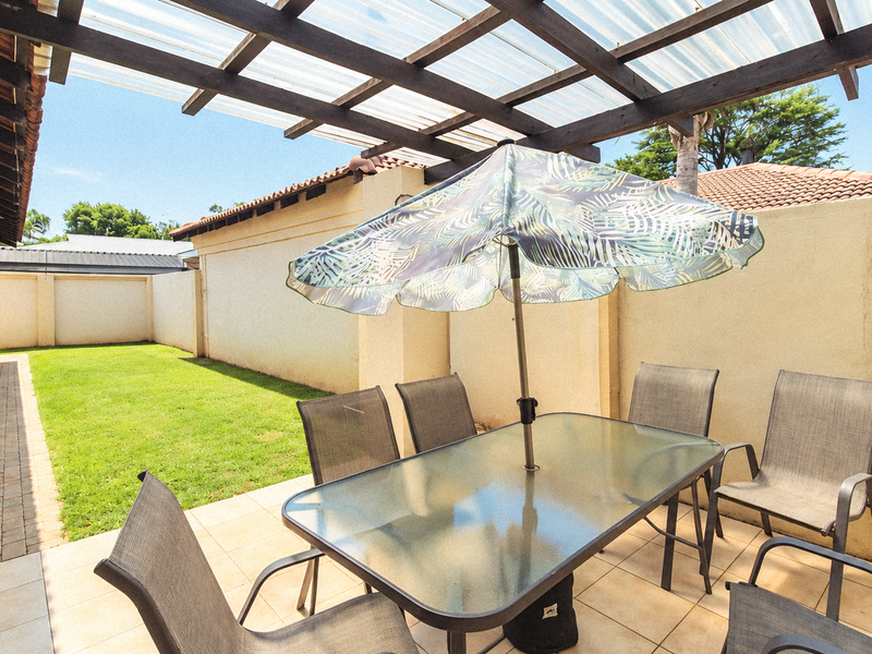 A covered patio area featuring a timber pergola with translucent roofing, tiled flooring, and direct access to a private rear garden space.