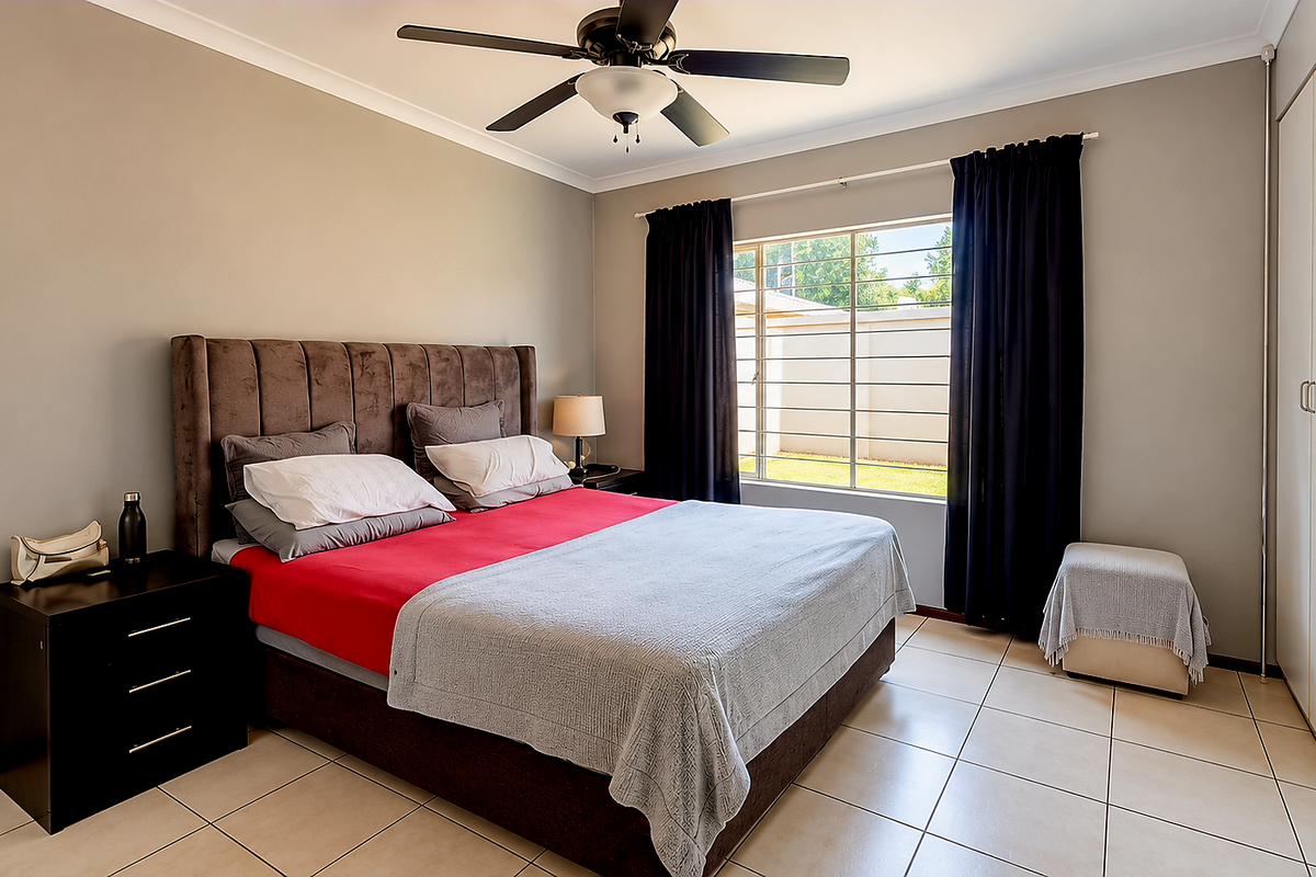 A well-maintained bedroom featuring tiled flooring, built-in cupboards, a ceiling fan, and security bars on the window.