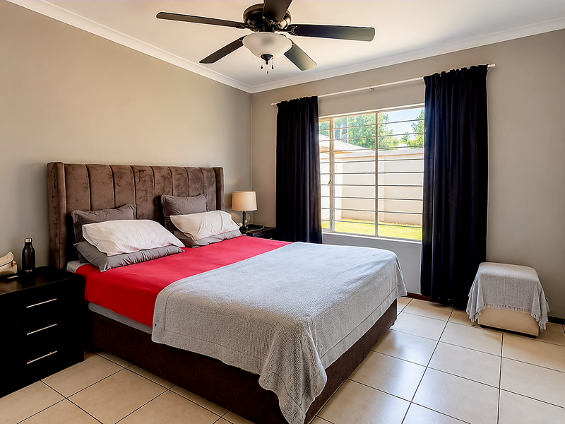 A well-maintained bedroom featuring tiled flooring, built-in cupboards, a ceiling fan, and security bars on the window.