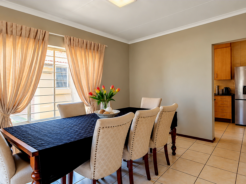 A bright dining room featuring neutral walls, tiled flooring, and a seamless transition into the adjacent kitchen area.