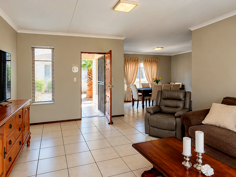 Spacious open-plan living and dining area featuring neutral wall tones, tiled flooring, and direct access to an outdoor patio through a security gate.