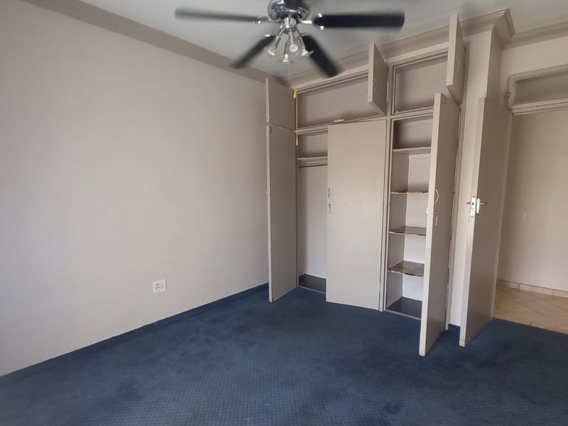 An empty bedroom featuring built-in cupboards, a ceiling fan, and blue carpeting, offering a blank canvas for personalization.