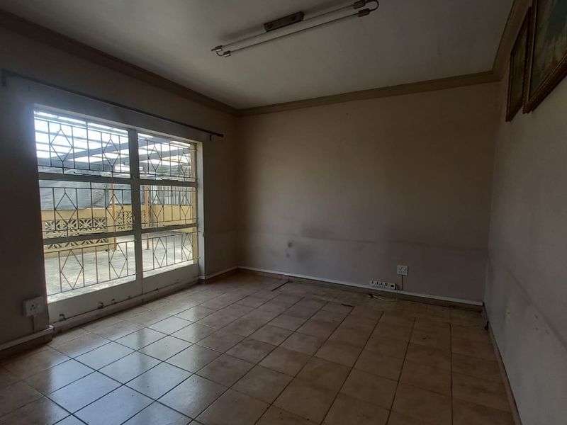 An empty living room featuring tiled flooring, a large window with security bars, and a fluorescent ceiling light, requiring cosmetic updates to the walls.
