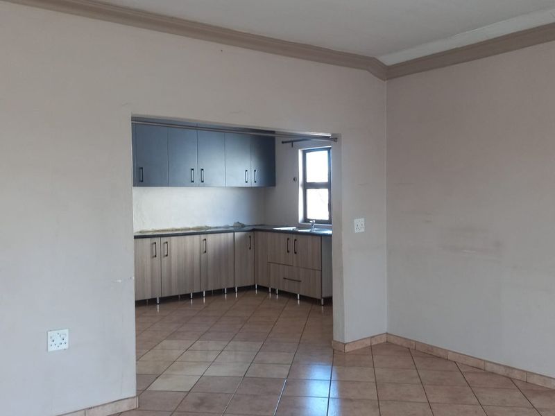 An open-plan living area featuring tiled flooring and a separate kitchen space with built-in cabinetry and a sink.