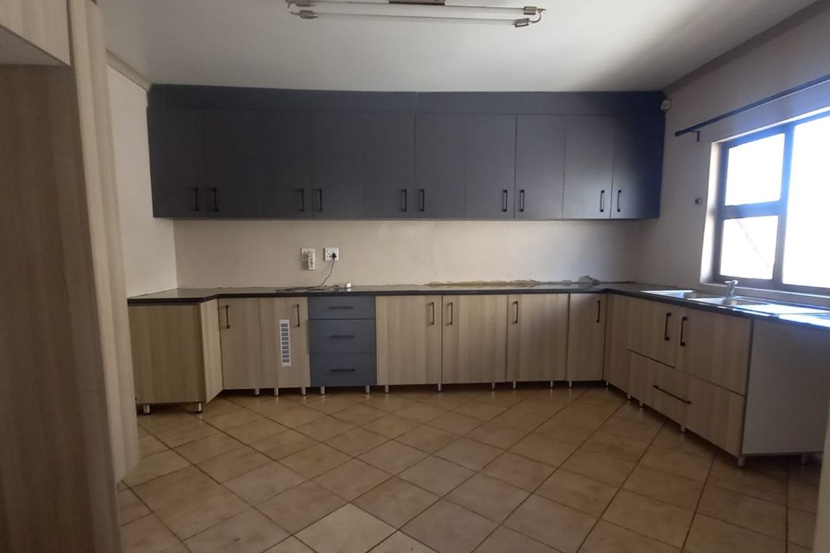 An empty kitchen featuring two-tone cabinetry, laminate countertops, a double sink, and ceramic floor tiles, awaiting final finishes and appliances.