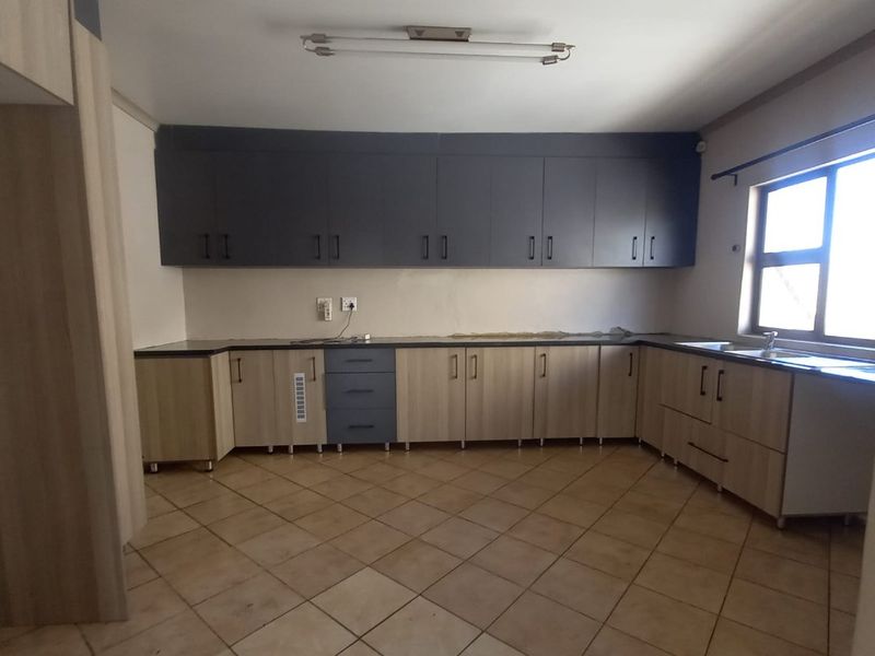 An empty kitchen featuring two-tone cabinetry, laminate countertops, a double sink, and ceramic floor tiles, awaiting final finishes and appliances.
