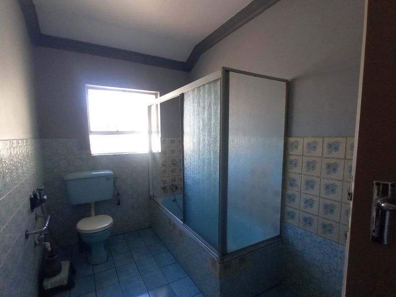 A dated bathroom featuring a built-in bathtub with a shower screen, a toilet, and blue tiled finishes throughout.