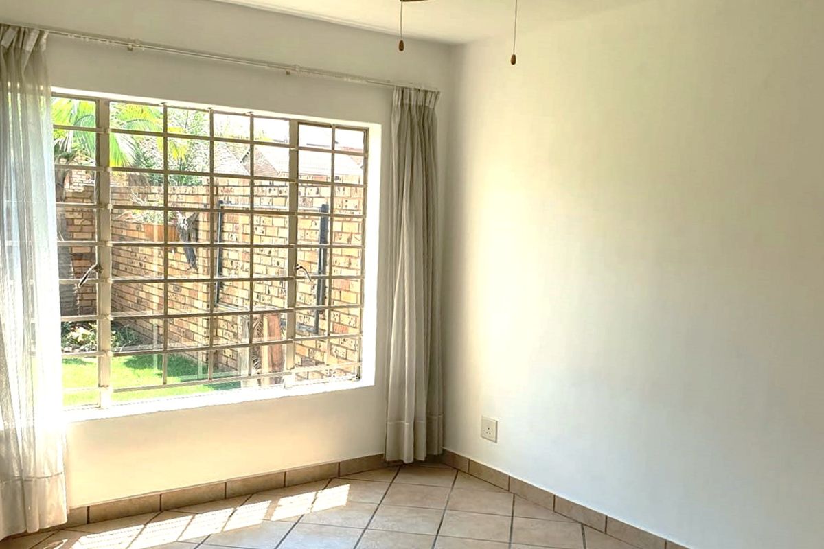 A bright, empty bedroom featuring tiled flooring and a large window fitted with security bars, offering a view of the rear garden area.