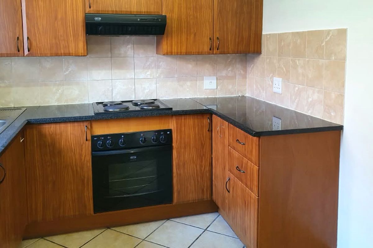 A functional kitchen featuring wood-look laminate cabinetry, dark granite countertops, built-in oven, electric hob, and a neutral ceramic tile backsplash.