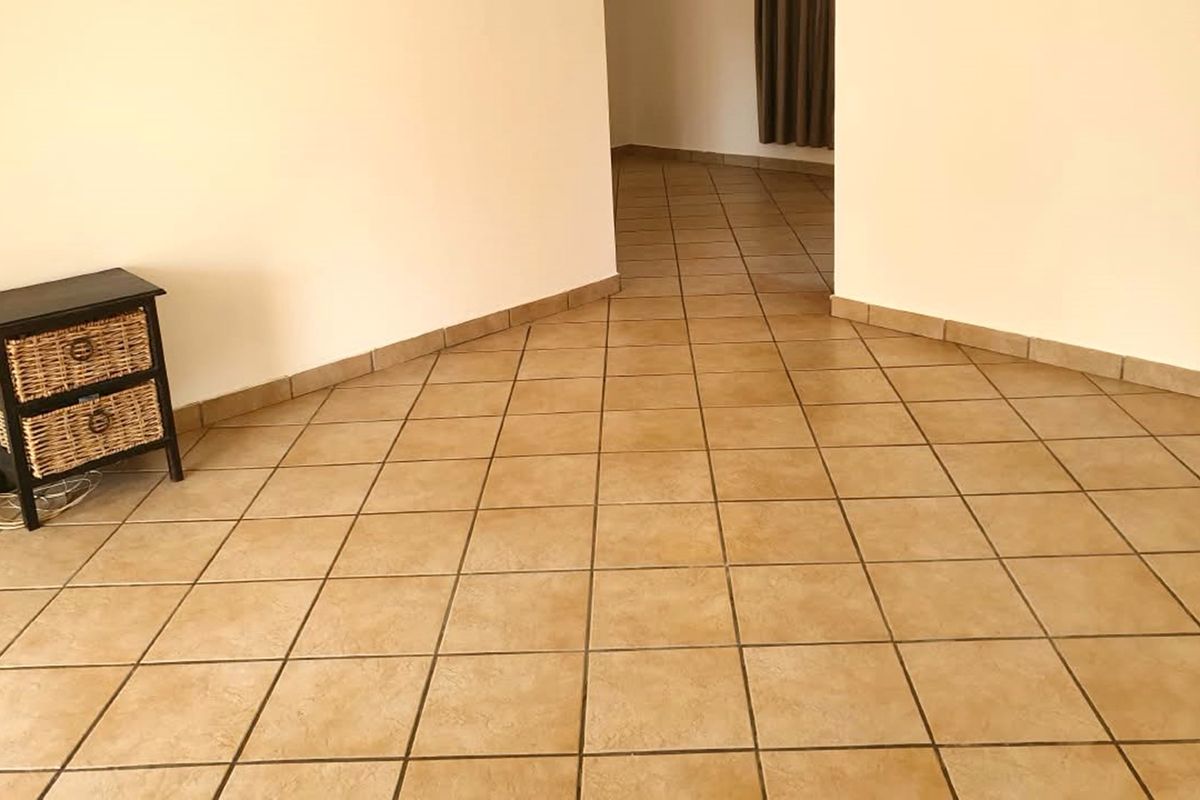An empty living area featuring neutral tiled flooring and matching tiled skirting boards, providing a clean and versatile space.