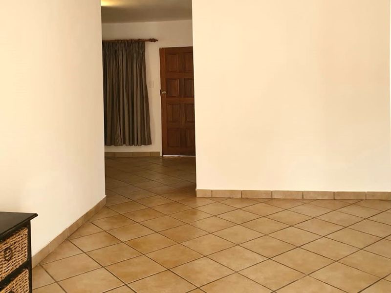 A spacious, empty hallway featuring neutral walls and classic ceramic floor tiles, leading towards a timber door.