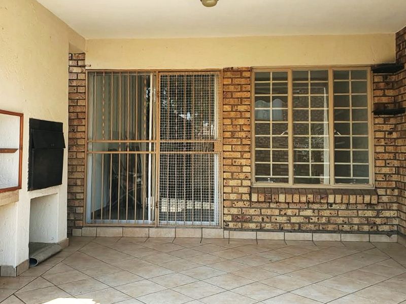 Covered patio area featuring a built-in braai, tiled flooring, and secure access points with security gates and bars.