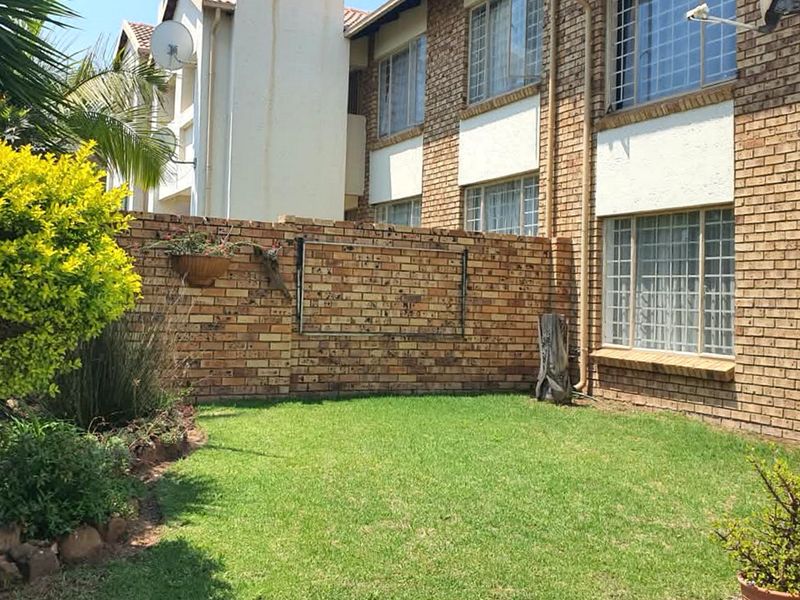 A private rear garden area featuring a well-maintained lawn and face brick townhouse exterior with security-fitted windows.