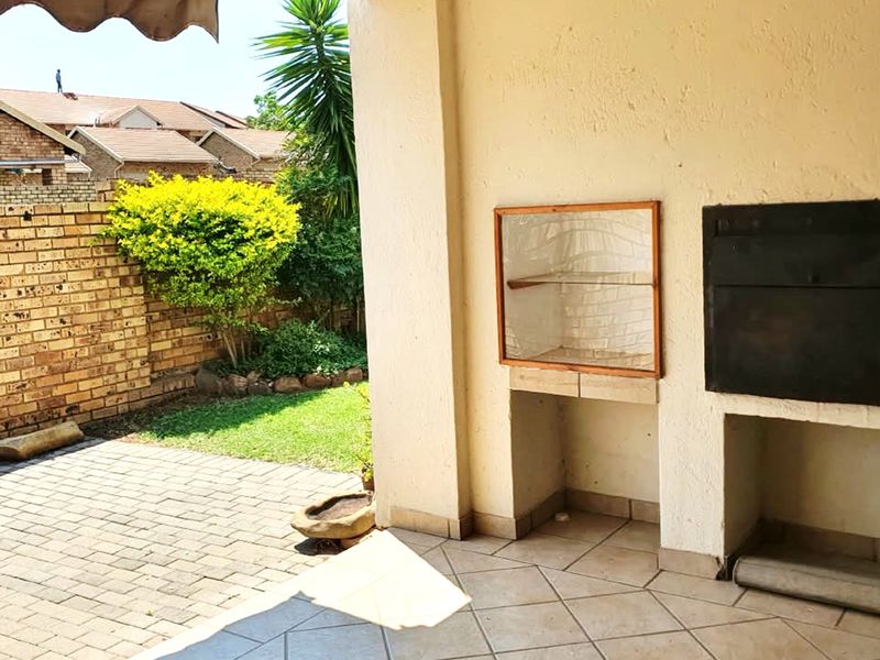 Covered patio area featuring a built-in braai, paved flooring, and direct access to a private garden with brick boundary walls.