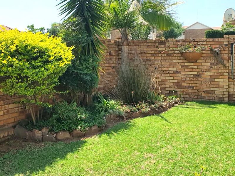 A private rear garden featuring a well-maintained lawn, established garden beds, and a sturdy face-brick boundary wall.
