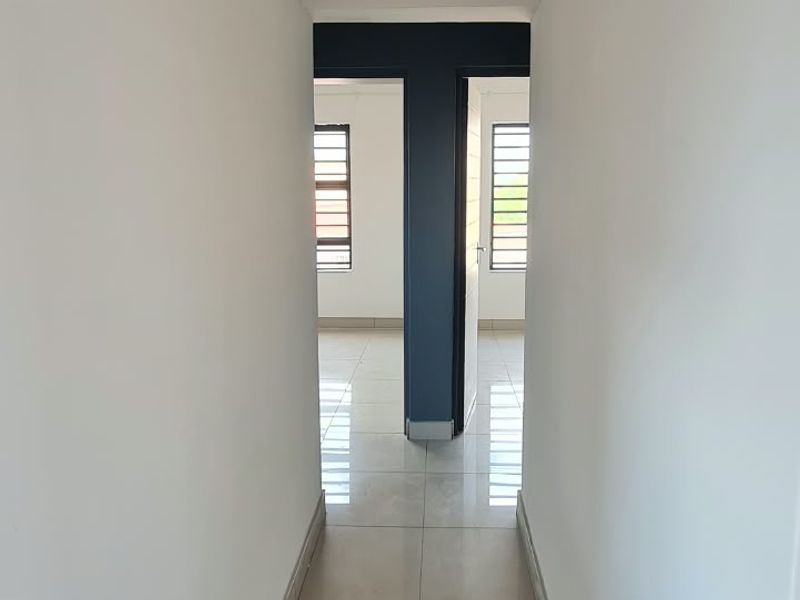 A clean, empty hallway featuring neutral tiled flooring and recessed ceiling lighting, providing access to adjacent rooms.