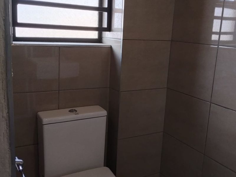 A compact bathroom featuring neutral wall tiling, a modern toilet, and a window fitted with security bars for added safety.