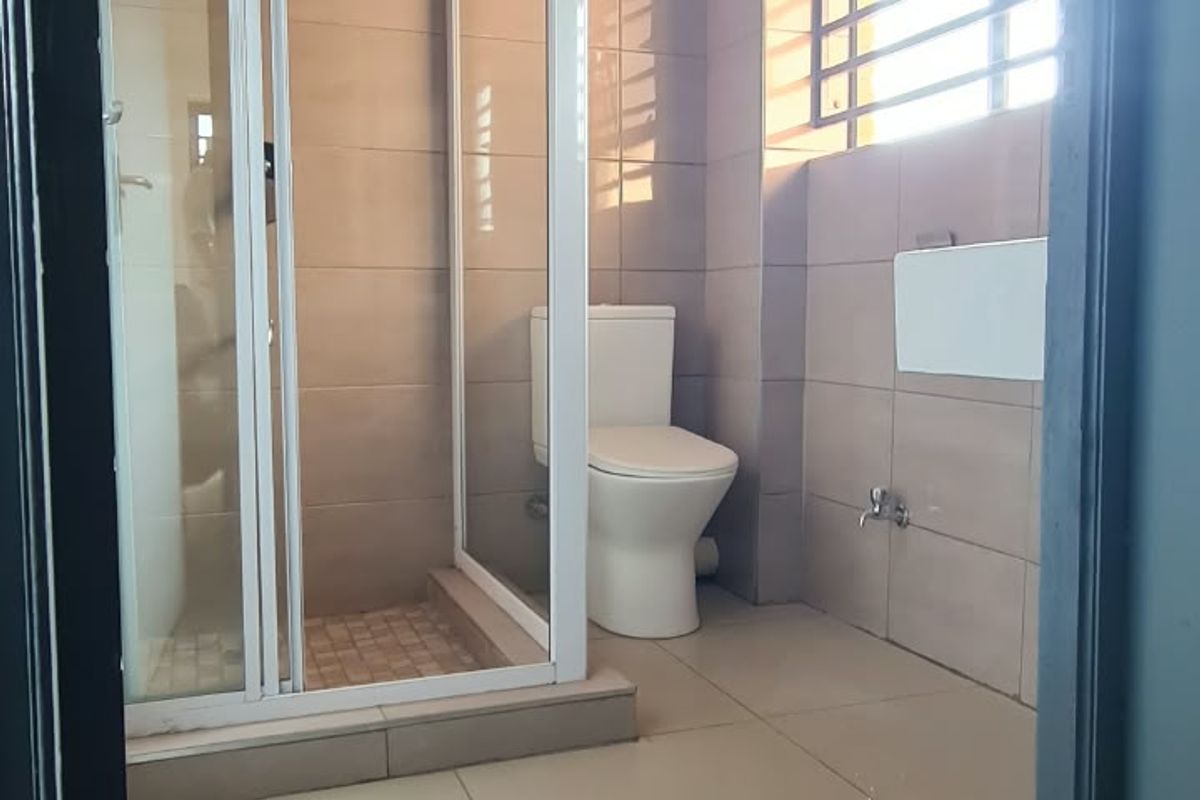 A clean, modern bathroom featuring a glass-enclosed shower, tiled walls and flooring, and a window with security bars.