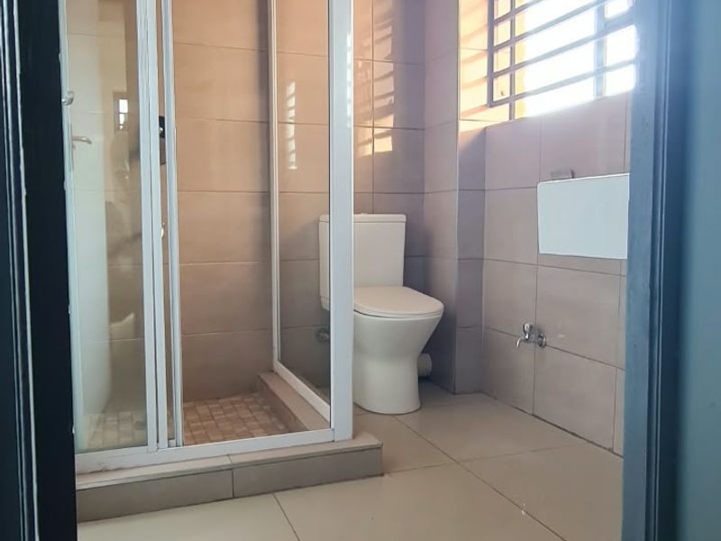 A clean, modern bathroom featuring a glass-enclosed shower, tiled walls and flooring, and a window with security bars.