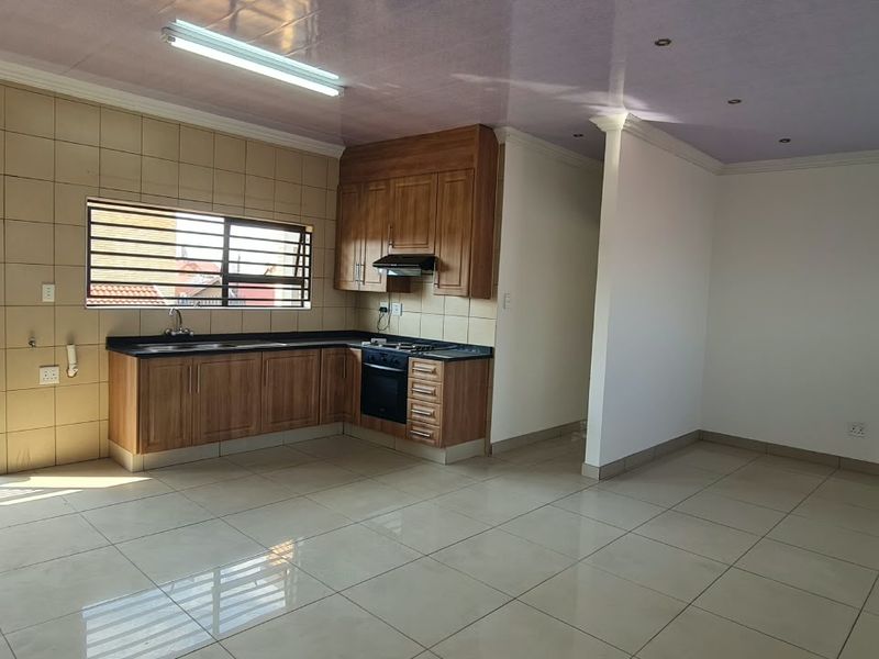Spacious open-plan living area featuring a functional kitchen with wooden cabinetry, black granite countertops, and tiled flooring throughout.