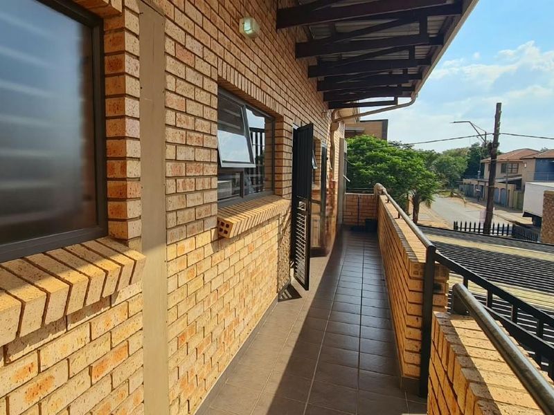A spacious outdoor balcony featuring exposed brick walls, tiled flooring, and a protective awning, offering a clear view of the surrounding neighborhood.