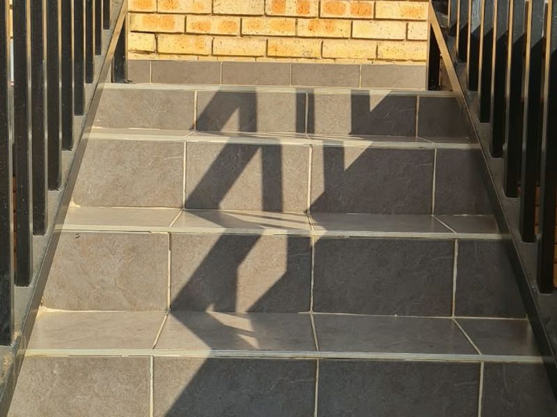 An exterior entrance featuring a tiled staircase with metal handrails leading up to a face brick facade with a louvre window.