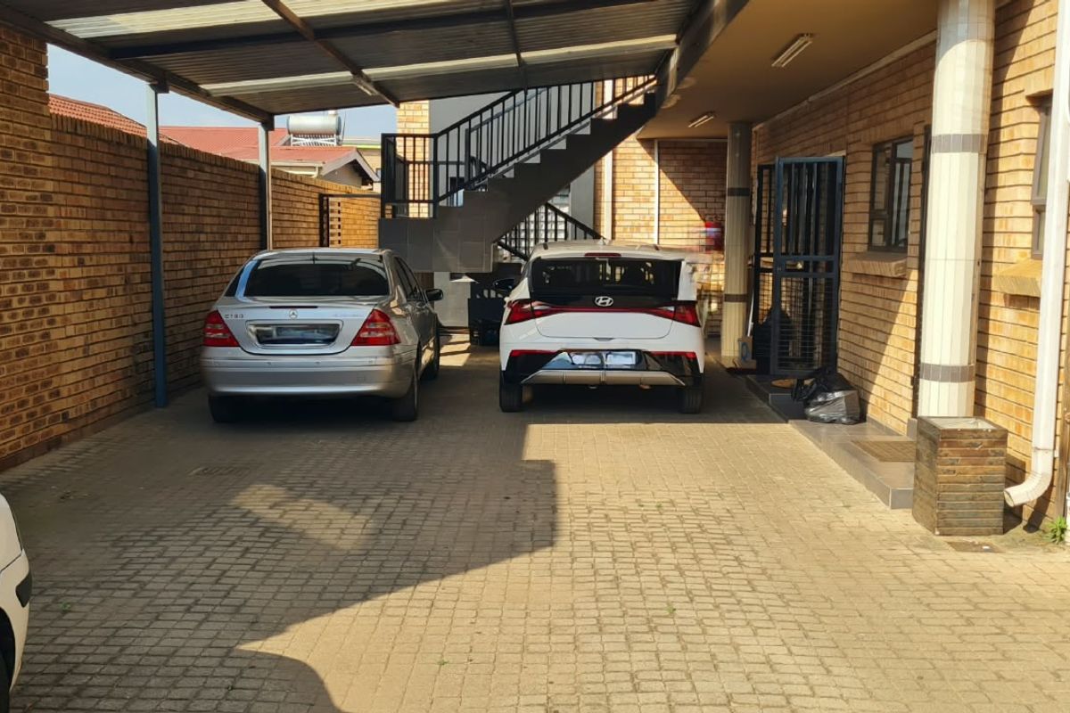 A covered parking area featuring brick walls, a paved driveway, and an external metal staircase leading to upper levels.