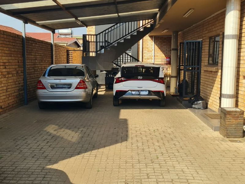 A covered parking area featuring brick walls, a paved driveway, and an external metal staircase leading to upper levels.