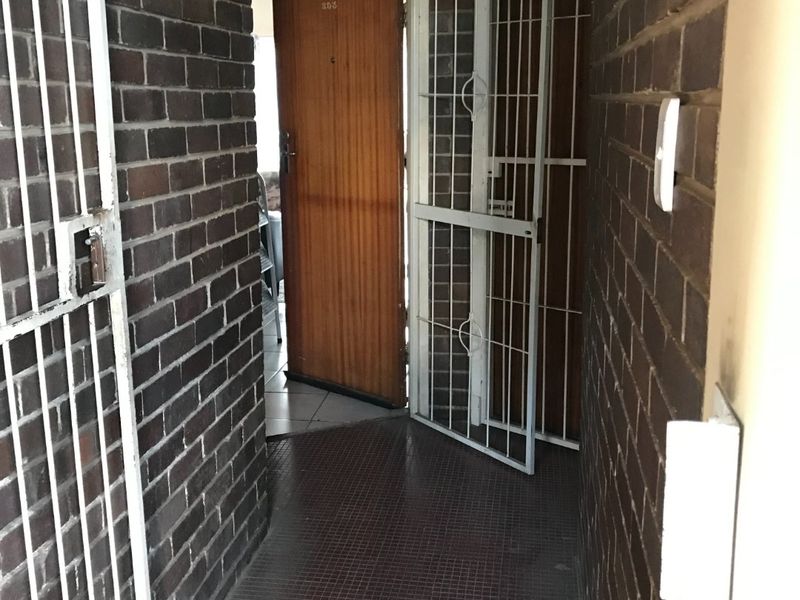 An apartment entrance featuring exposed brick walls, tiled flooring, and a secure metal gate leading to a wooden front door.