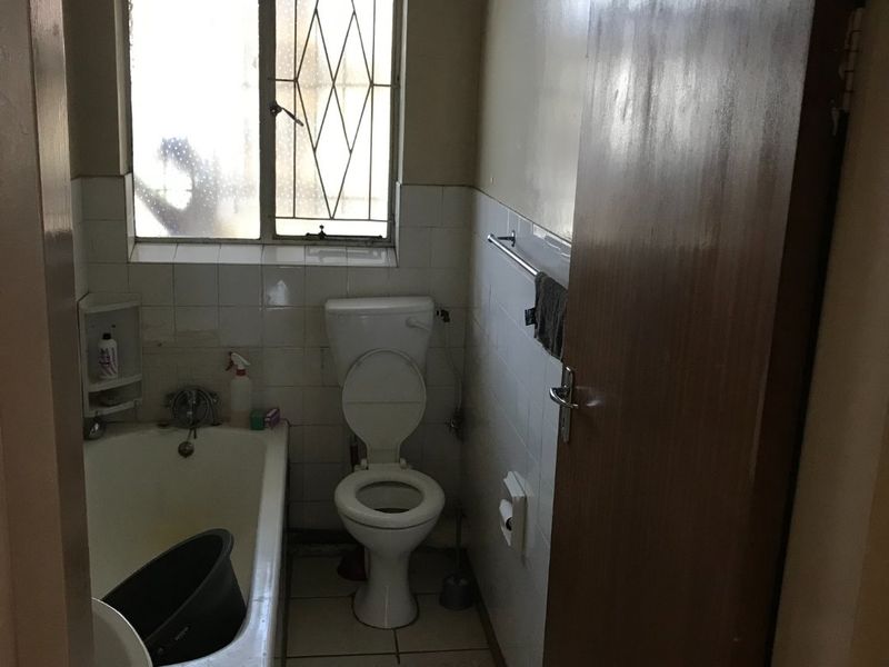 A compact bathroom featuring a standard bathtub, toilet, and tiled finishes, requiring cosmetic updates to improve its overall condition and appeal.