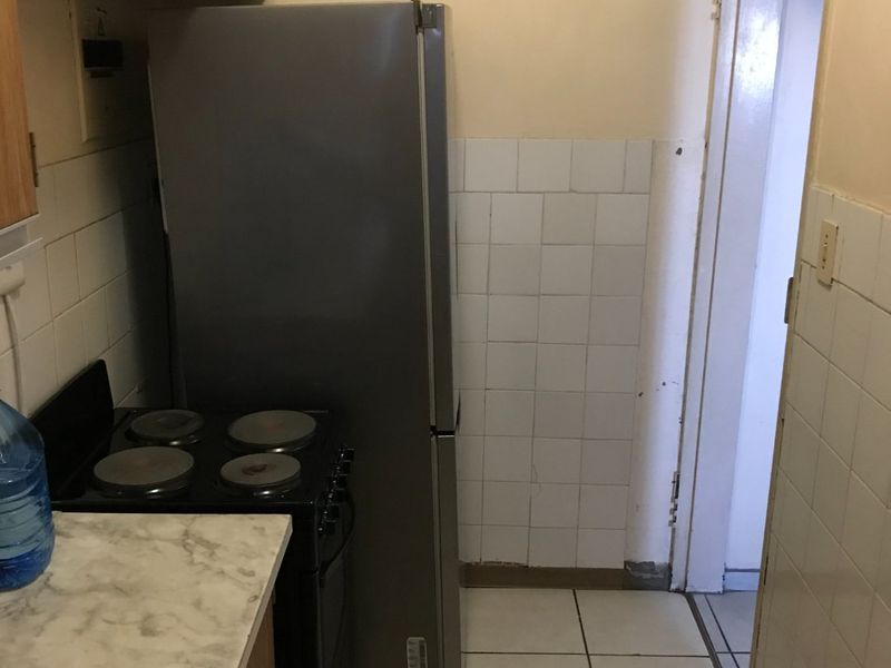 A compact kitchen area featuring tiled flooring, a tiled splashback, and basic cabinetry, currently requiring cosmetic updates and maintenance to improve its overall condition.