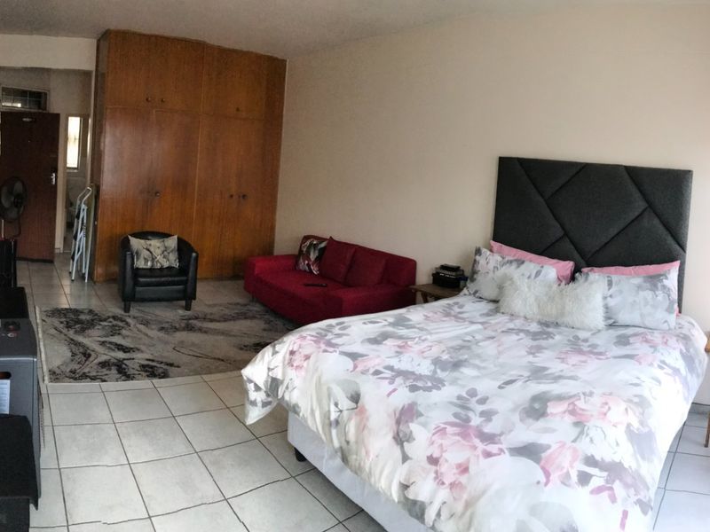 A bedroom featuring tiled flooring and built-in wooden cupboards, offering a functional layout with space for a seating area.