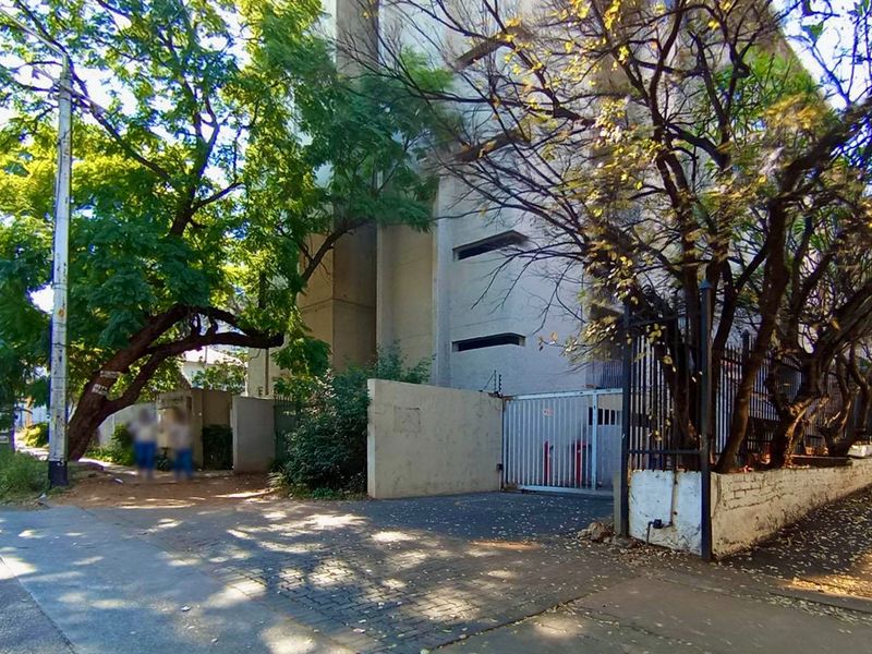 Street-level view of the apartment complex entrance featuring a security gate, perimeter wall, and paved driveway access.