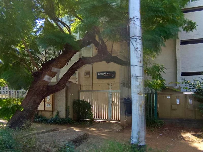 Street-level view of the Capital Hill apartment complex entrance, featuring a security gate, electric fencing, and concrete building facade.